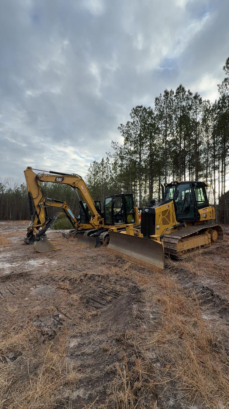 Excavators and a dozer on a freshly cleared lot, with the tree line left standing.
