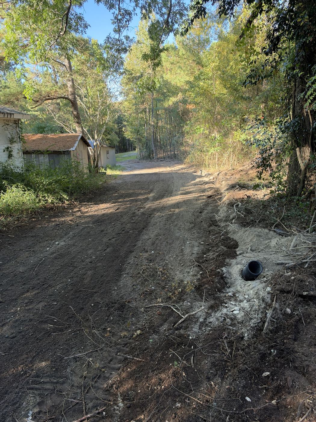 Regraded access drive with a drain pipe set in gravel at the edge.