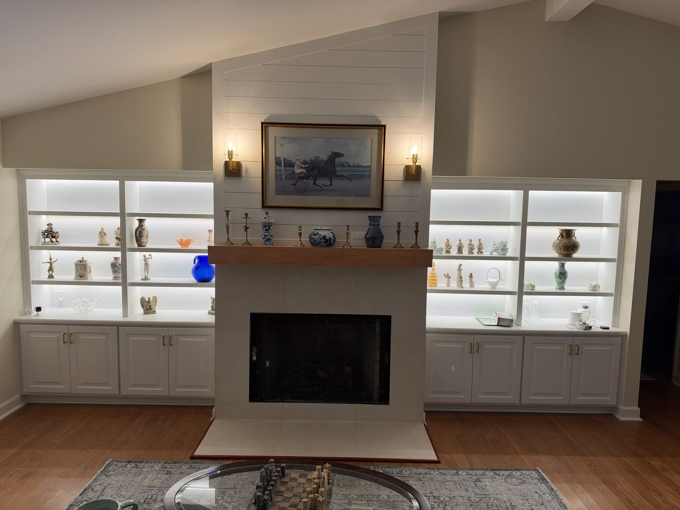 Shiplap fireplace wall with lit built-in shelving and cabinets on both sides.